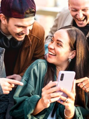 Group of young people laughing and pointing at a girl's phone